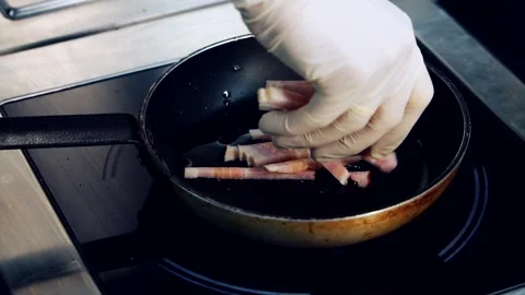 Frying bacon in the restaurant. Bacon pieces fry in a pan. Chef's hand in glove Stock Footage 318310378