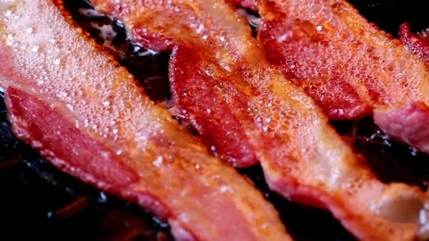 Frying bacon slices on a pan in kitchen for breakfast. Closeup of Frying Bacon. 스톡 동영상 334642306