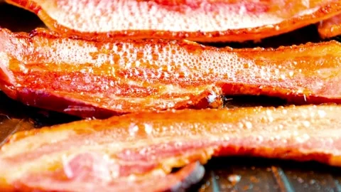 Frying bacon slices on a pan in kitchen for breakfast. Closeup of Frying Bacon. 스톡 동영상 334642307
