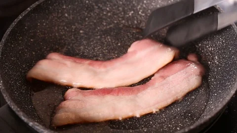 Frying bacon strips in a black pan Stock Footage 129230281