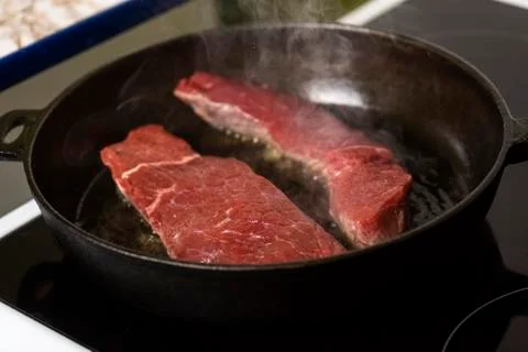 Frying beef steaks on a cast-iron pan Stock Photos