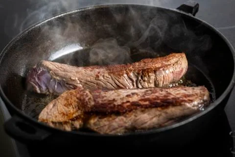Frying beef steaks on a cast-iron pan Stock Photos