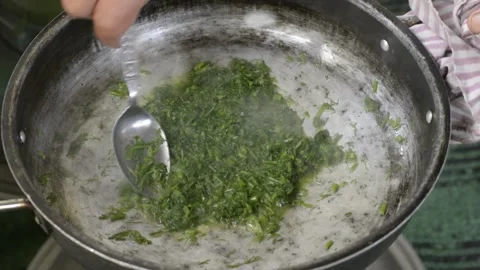 Frying chopped fresh dill plants inside old pan on oven Stock Footage 131196851