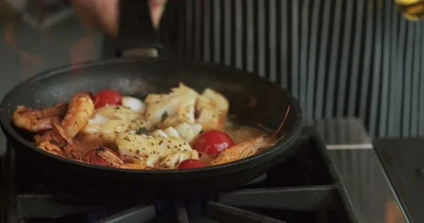 Frying the cod with tiger shrimps, shallots and cherry tomatoes on a pan Stock Footage 88981131