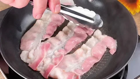 Frying crispy bacon strips in a hot pan for a delicious breakfast meal Stock Footage 325032724