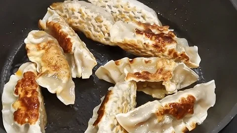 Frying dumplings in a black iron pan under artificial light. 库存影片 113687149