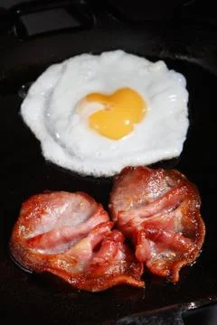 Frying egg and bacon rashers Stock Photos