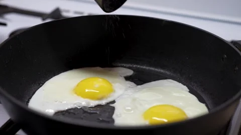Frying Egg in a Cooking Pan, close-up. Man hands applying salt on eggs from.. Stock Footage 272156165