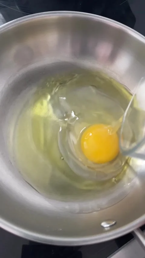 Frying an Egg in Olive Oil on a Stainless Steel Pan Stock Footage 299727012