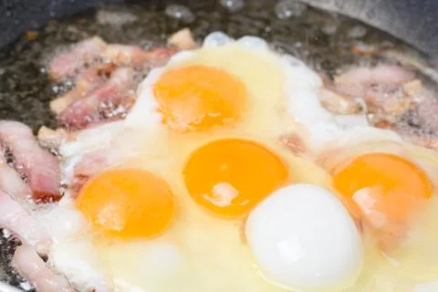 Frying eggs with sliced bacon in the hot oil Foto stock