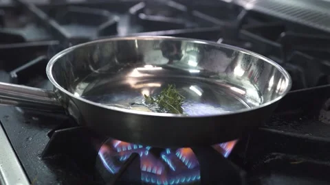 Frying fresh thyme in large pan on contemporary stove Stock Footage 143114713