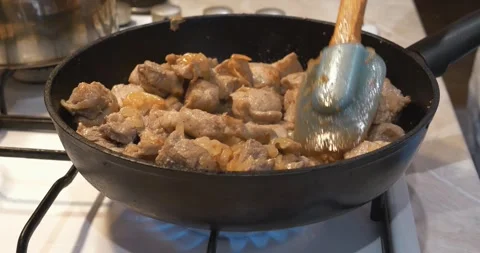 Frying meat. Cook stirs pieces of meat with onion in frying pan on a stove Stock Footage 318418894