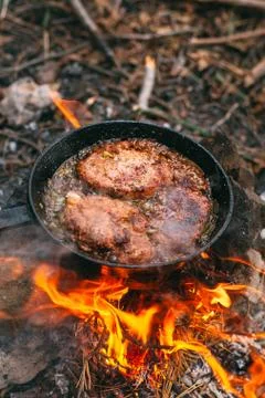 Frying meat in a pan over an open fire with leek. Steak in a pan on a fire. C Stock Photos