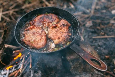 Frying meat in a pan over an open fire with leek. Steak in a pan on a fire. C Stock Photos