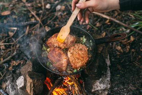 Frying meat in a pan over an open fire with leek. Steak in a pan on a fire. C Stock Photos