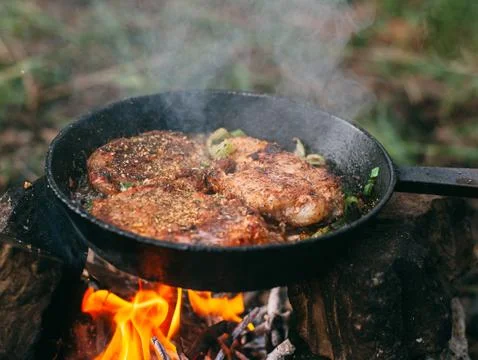 Frying meat in a pan over an open fire with leek. Steak in a pan on a fire. C Stock Photos