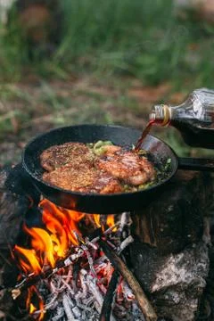 Frying meat in a pan over an open fire with leek. Steak in a pan on a fire. C Stock Photos