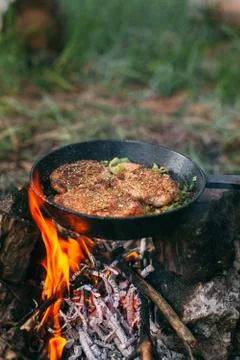 Frying meat in a pan over an open fire with leek. Steak in a pan on a fire. C Stock Photos