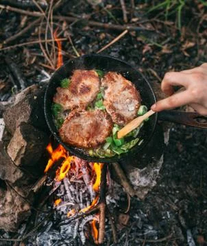 Frying meat in a pan over an open fire with leek. Steak in a pan on a fire. C Stock Photos