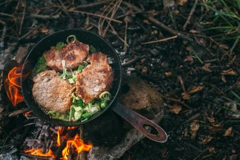 Frying meat in a pan over an open fire with leek. Steak in a pan on a fire. C Stock Photos