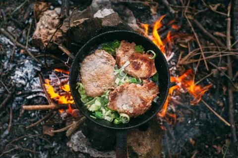 Frying meat in a pan over an open fire with leek. Steak in a pan on a fire. C Stock Photos