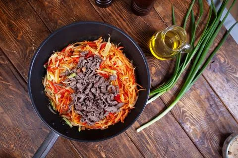 A frying pan with assorted meat, fresh vegetables, and a wooden spoon Stock Photos