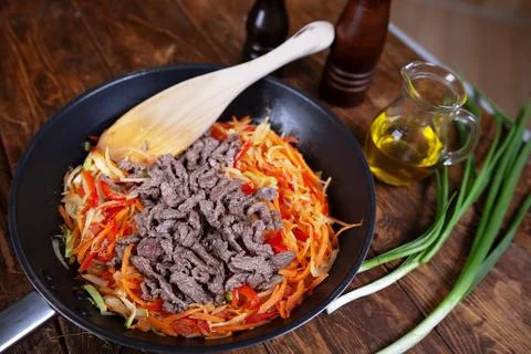A frying pan with assorted meat, fresh vegetables, and a wooden spoon Stock Photos