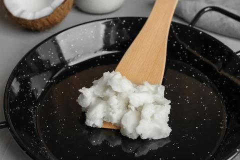 Frying pan with coconut oil and wooden spatula on light grey table, closeup Stock Photos