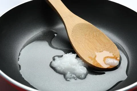 Frying pan with coconut oil and wooden spoon, closeup. Healthy cooking Stock Photos