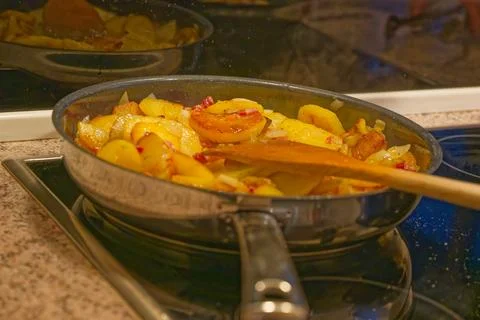 Frying pan with cooked potatoes and onions on kitchen stove with wooden spatu Stock Photos