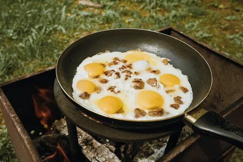Frying pan of fried eggs and bacon, green grass on the background, cooked on the 스톡 사진