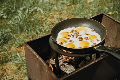 Frying pan of fried eggs and bacon, green grass on the background, cooked on the Stock Photos