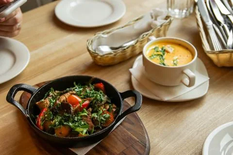 A frying pan with fried meat and vegetables in the foreground stands on a woo Stock Photos