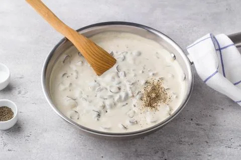 Frying pan with fried mushrooms with onions in bechamel sauce on a gray tex.. Foto stock