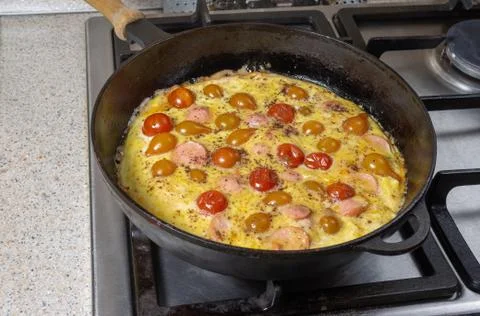 Frying pan full of omelet with cherry tomatoes and sausage slices standing on Stock Photos