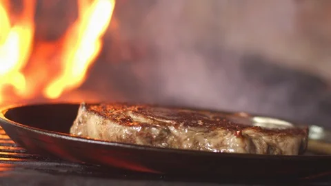 A frying pan with a juicy steak in the foreground, a piece of butter dripping Stock Footage 124709767