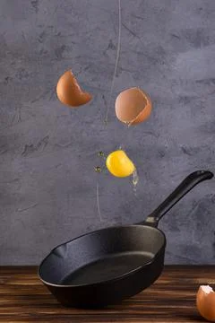 Frying pan with levitation raw egg shell on wooden table Stock Photos