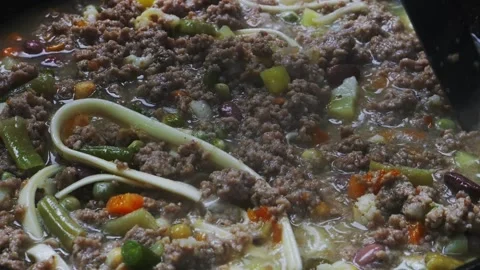 In a frying pan with minced meat and vegetables, stir the udon with a spoon.. Video stock 297098207