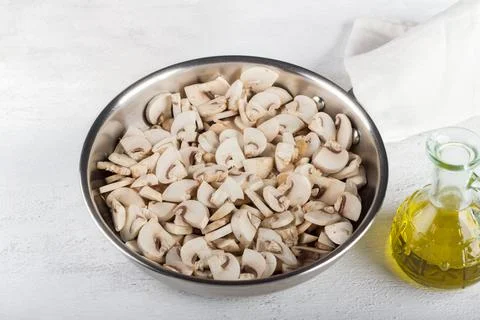 Frying pan with raw chopped champignons mushrooms on a light gray backgroun.. Stock Photos