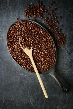 Frying pan with roasted coffee beans and wooden stirring spoon, top view Stock Photos