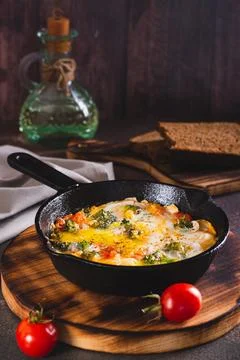 Frying pan with scrambled eggs with broccoli and tomatoes on a wooden board.. Stock Photos