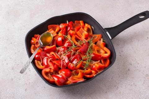 Frying pan with stewed sliced red bell pepper, onion, fresh thyme and honey.. Stock Photos