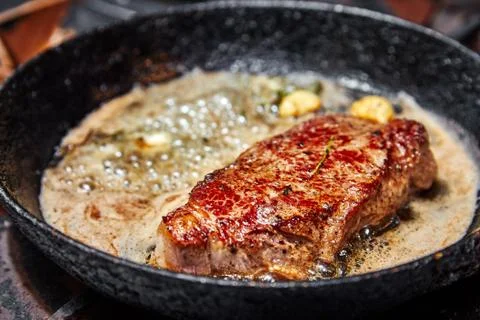 Frying pan on a stove on which a large piece of meat is fried with butter Stock Photos