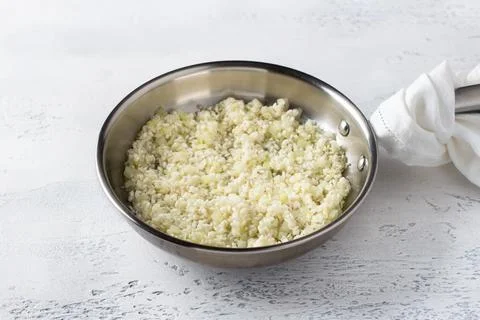 Frying pan with uncooked rice and onions on a light blue background. How to.. Stock-Fotos