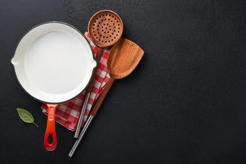 Frying pan white , black empty plate, basil leaves and spices on dark stone b Stock Photos