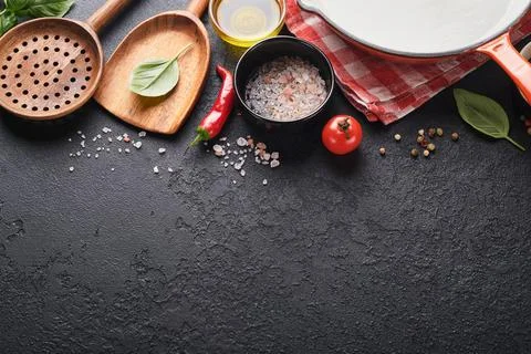 Frying pan white , black empty plate, basil leaves and spices on dark stone b Stock Photos