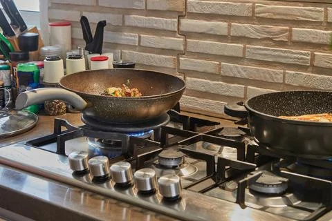 Frying pans with fried potatoes, chestnuts, parsley, parmesan on gas stove .. Фото