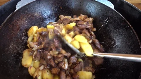 Frying of potatoes with meat, onions and tomatoes in a kazan on a gas grill Stock Footage 84154030