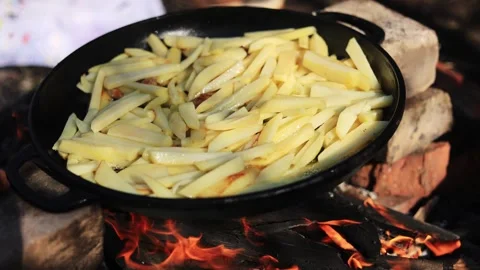 Frying Potatoes in a Pan Over an Open Campfire for a Rustic Meal Stock Footage 338997989