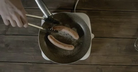 Frying sausages in a pan for breakfast. A meat crispy sausages are fried in a Stock Footage 251546221